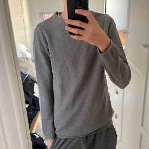 Grå långärmad tröja Kronstadt - Säljer en stilren grå långärmad tröja från Kronstadt i storlek S. Tröjan har en rund hals och är tillverkad i ett mjukt, stickat material med diskret struktur. Perfekt för dig som gillar enkel och clean look.