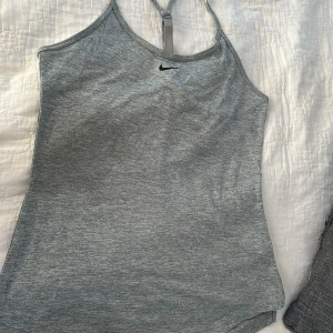 Grå Nike Dri-Fit linnetopp XS - Säljer en grå sportig linnetopp från Nike i Dri-Fit-material. Toppen har smala axelband med snygg detalj i ryggen och en liten svart Nike-logga framtill. Perfekt för träning eller när du vill ha en luftig och bekväm look.ALDRIG använt ba testat ligger på 459kr i ordinarie men säljer för 200kr