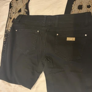 Svarta skinny jeans från MET, strl 29 - Svarta skinny jeans från MET med snygga detaljer som guldknappar med stenar och guldfärgad logga på bakfickan. Jeansen är tillverkade i bomull med lite stretch för skön passform. Klassisk femficksmodell och smal siluett.