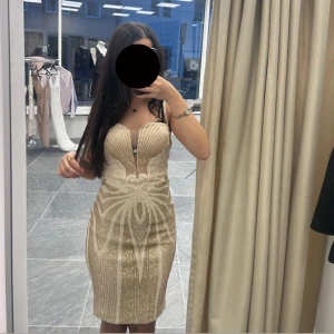 Glittrig champagnefärgad kortklänning - Säljer en glittrig och figurnära kortklänning i champagnefärg med snygga mönster och pärldetaljer.  Klänningen finns i alla storlekar XS-XL, Pris går att diskutera.