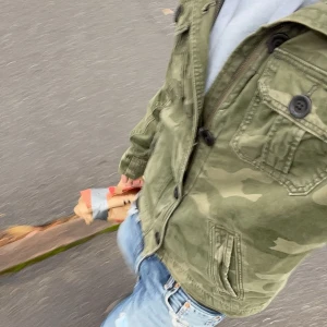 Camouflage jacka från Hollister - Snygg militärgrön camouflage jacka från Hollister med klassisk krage, knappar och dragkedja framtill. Jackan har två bröstfickor med knappar och två snedställda fickor. Perfekt för dig som vill ha en streetig look.