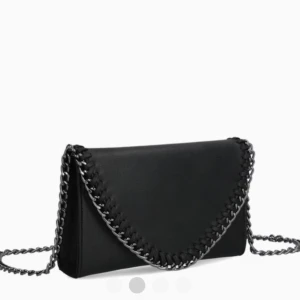 Svart kuvertväska med kedja - Stilren svart kuvertväska med silverfärgad kedja som axelrem och snygga kedjedetaljer längs kanten. Väskan har en klassisk kuvertform och är tillverkad i ett slätt material som liknar skinn. Perfekt för dig som vill ha en edgy och trendig accessoar. Från tiamo.