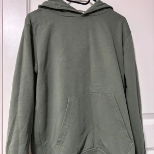 Grön hoodie från Kappahl - Säljer en stilren grön hoodie från Kappahl i storlek 158/164. Tröjan har en klassisk huva, känguruficka framtill och är tillverkad i mjuk bomullsmix. Perfekt för chill dagar eller när du vill ha en enkel och snygg look.