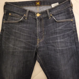 Mörkblå jeans från Lee W32 L32 - Snygga mörkblå jeans från Lee med klassisk femficksdesign och guldfärgade nitar. Shortsen har normal passform och är tillverkade i slitstark bomull. Perfekta för en avslappnad stil med en cool denimlook.