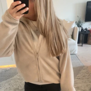 Beige fleece hoodie med dragkedja - Mysig beige hoodie i fleece med hel dragkedja framtill. Tröjan har en avslappnad passform och huva, perfekt för kyliga dagar. Enkel och stilren design som passar till det mesta.