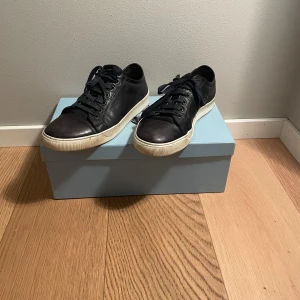 Svarta sneakers från Lanvin i skinn - Svarta sneakers från Lanvin med vit platt sula och snörning. Skorna är tillverkade i skinn och har en klassisk rund tå. Snygg kontrast mellan svart ovandel och vit sula, perfekt för dig som gillar stilrena och tidlösa sneakers.