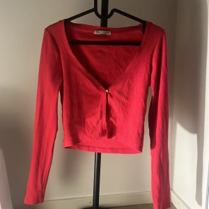 Rosa croppad topp från Zara - Säljer en rosa croppad topp från Zara med lång ärm och v-ringad hals. Toppen har en liten knapp framtill och är ribbad i materialet för extra cool vibe. Perfekt att styla med jeans eller kjol för en trendig look.