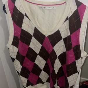 Tommy Hilfiger slipover - Snygg väst från Tommy Hilfiger i storlek XXL med klassiskt rutig mönster i brunt, rosa och vitt. V-ringad modell med ribbade kanter. Perfekt för lager-på-lager och en preppy stil.