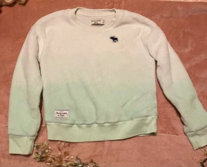 Ljusgrön fleece-tröja Abercrombie Kids - Supermjuk och fluffig fleece-tröja från Abercrombie Kids i ljusgrön och vit toning. Bra skick, inga defekter!
