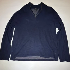 Marinblå långärmad tröja CK - Snygg marinblå långärmad tröja från Calvin Klein med half zip och ståkrage. Tröjan är i mjuk bomull och har en stilren, enkel design som passar perfekt till jeans eller chinos. Perfekt för dig som gillar klassisk och clean stil.