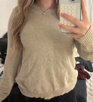 Beige stickad tröja med rund hals - Mysig beige stickad tröja med rund hals och ribbade muddar vid ärmslut och nederkant. Perfekt för dig som gillar en enkel och clean look. Långärmad modell som passar till jeans eller kjol. Snygg att styla med smycken eller lager på lager.