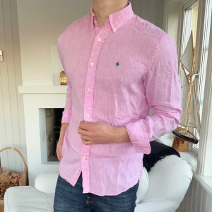 Rosa linneskjorta från Morris - Fräsch rosa skjorta från Morris i ren linne, perfekt för dig som gillar stilren och chill look. Klassisk krage, knappar hela vägen och långärmad modell. Diskret Morris-logga broderad på bröstet. Skjortan har en normal passform och känns lätt och luftig.