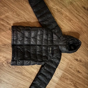 Svart dunjacka Peak Performance S - Svart dunjacka från Peak Performance i storlek S. Förutom hålen/defekterna som syns på sista bilden så är den i väldigt bra skick. Skriv för fler bilder✨