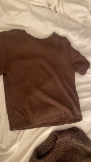 Brun stickad kortärmad tröja - En enkel brun stickad tröja med korta ärmar och rund hals. Tröjan har en clean look utan mönster eller detaljer, perfekt för dig som gillar basic och jordnära färger. Materialet är mjukt och skönt mot huden. Ett hål i högra armhålan 