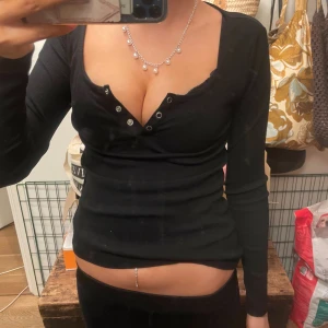 Svart ribbad långärmad topp - Säljer en svart långärmad topp från Anna field med ribbad struktur och djup v-ringning med knappar framtill. Toppen är tight och har en croppad passform som framhäver midjan. Perfekt för dig som gillar en stilren och edgy look. Använd ett par fåtal gånger!