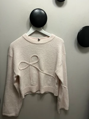 Ljusrosa stickad tröja med rosett från HM - Superfin ljusrosa stickad tröja från Gina Tricot med en dekorativ rosett framtill. Tröjan har en croppad passform, ribbade muddar och långa ärmar. Perfekt för dig som gillar söta detaljer och mjuka material.