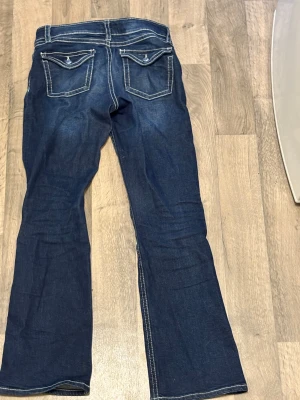 Mörkblå bootcut jeans med kontrastsömmar - Snygga mörkblå jeans med bootcut passform och tydliga vita kontrastsömmar. Jeansen har klassiska fickor med lock och knapp bak, samt en låg midja. Materialet är jeans och de har en cool, avslappnad vibe.