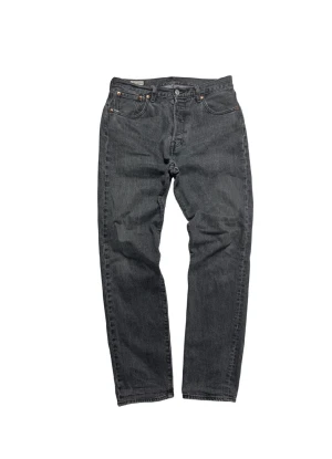 Levi's 501 grå jeans straight fit - Snygga grå Levi's 501 jeans med klassisk straight fit och fem fickor. Jeansen har en mörkgrå tvätt, knappgylf och ikonisk läderpatch bak i midjan. Passar dig som gillar tidlös stil och vill ha ett par jeans som funkar till allt.