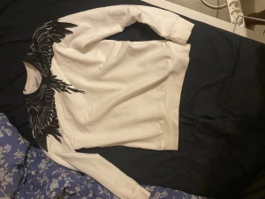 Vit sweatshirt från Marcelo Burlon - Vit sweatshirt från Marcelo Burlon County of Milan med svart grafiskt fågelmönster runt halsen och axlarna. Tröjan har långärmad passform och är tillverkad i mjuk bomull. Perfekt för dig som gillar streetwear med unik design.