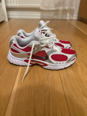 Nike sneakers röd och silver mesh - Nike sneakers med röd mesh, silverdetaljer och vita inslag. Skorna har en sportig design med vit sula, snörning och svart swoosh på sidan. Ovandelen är tillverkad i syntet och mesh för bra ventilation. Perfekt för dig som gillar färgstarka och trendiga sneakers.