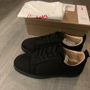 Louboutin skor - Snygga svarta sneakers från Christian Louboutin med klassisk röd sula och diskret logga undertill. Skorna har rund tå, svart snörning och mjukt beige foder inne i skorna. Yttermaterialet är i skinn och textil, vilket ger en stilren och lyxig känsla. Helt nya skit feta och allt ingår:låda, påse mm. 