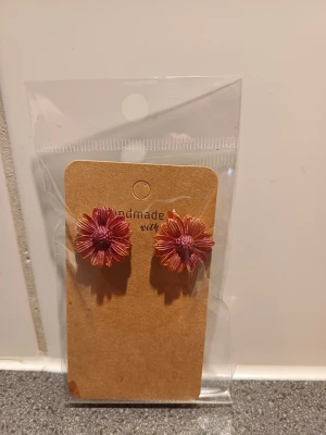 Blommiga örhängen i rosa och lila - Superfina handgjorda örhängen formade som blommor i rosa och lila toner. Perfekta för dig som vill ha en färgglad och unik detalj till din stil. Blommorna har tydliga kronblad och en markerad mitt, vilket ger ett coolt och lekfullt uttryck.