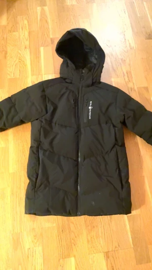 Svart Sail Racing dunjacka med huva - Säljer en svart Sail Racing PATROL dunjacka med huva och snygga logodetaljer på bröstet och ärmen. Den är storlek S (170) Jag kan posta eller överlämna!