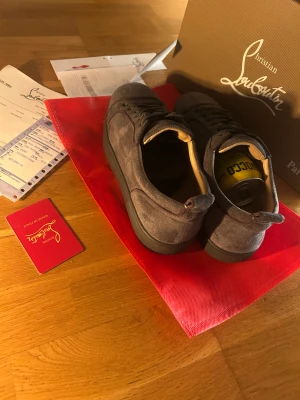 Grå mocka sneakers Christian Louboutin - Säljer ett par grå sneakers från Christian Louboutin i lyxig mocka med klassisk röd sula och rund tå. Skorna har snörning och diskreta detaljer, perfekt för dig som vill sticka ut med stil. Kommer med originalkartong och dustbag.
