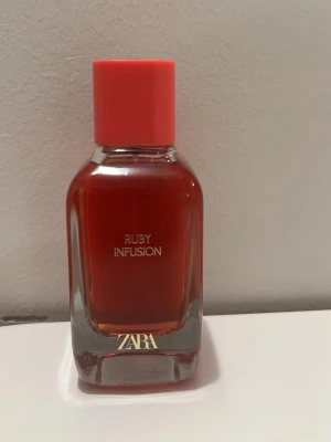 ZARA Ruby Infusion parfym 50ml - Ruby Infusion från ZARA är en parfym i en stilren glasflaska med rödtonad vätska och matchande röd kork. Flaskan har raka linjer och guldtext på framsidan. Perfekt för dig som gillar trendiga och moderna dofter.