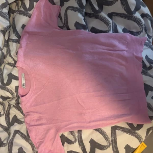 Ljusrosa kortärmad topp från Zara - Säljer en ljusrosa topp från Zara med korta ärmar och rund hals. Toppen har en mjuk, stickad känsla och ribbade kanter vid ärmslut och nederkant. Perfekt för en enkel och söt look.
