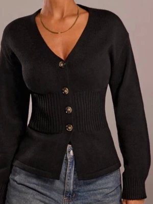 Svart ribbad kofta med knappar - Snygg svart kofta med ribbad midja och fyra dekorativa knappar framtill. Koftan har v-ringning och långa ärmar, perfekt att styla till jeans eller kjol. Materialet är stickat och ger en skön passform.