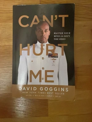Can’t Hurt Me av David Goggins - Boken 'Can’t Hurt Me' av David Goggins är en inspirerande berättelse om mental styrka och att övervinna motgångar. Omslaget är svart med guldiga bokstäver och visar en person i vit uniform. Pocketbok i papper, perfekt för dig som gillar starka livshistorier och motivation.