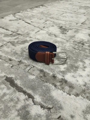 Blått flätat bälte med skin-detaljer - Vackert blått flätat bälte  Mått: 105 cm Lång 3.4 cm Bredd