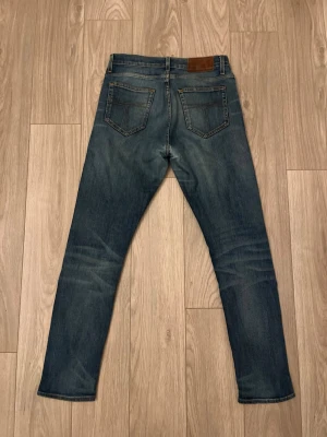 Tiger of Sweden Jeans - Snygga blå jeans med klassisk tvätt och raka ben. Jeansen har fem fickor, normal passform och subtila slitningar för en avslappnad look. Tillverkade i bomull med en skön jeanskänsla. Perfekta för dig som gillar en tidlös stil. Storlek 29/32