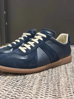 Blå sneakers med mockadetaljer - Snygga blå sneakers med både mocka och skinnpaneler, beige snörning och klassisk gummisula. Skorna har en låg profil och rund tå, vilket ger en clean och stilren look. Perfekta för dig som gillar en enkel men ändå trendig stil.