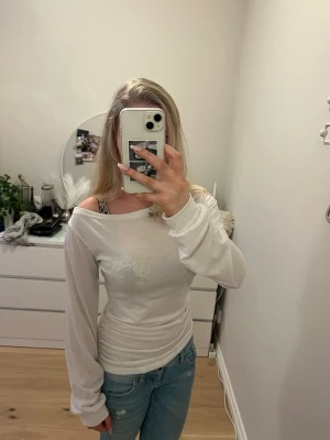 Vit off shoulder långärmad topp - Säljer en vit långärmad topp med off shoulder-skärning. Toppen är figurnära och har en enkel, stilren design utan synliga loggor eller mönster. Tillverkad i mjukt och stretchigt material som sitter snyggt på kroppen. Perfekt att styla med jeans eller kjol. Den är i storlek xs men sitter mycket mer som en s nästan m skulle jag säga 