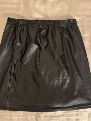 Svart kort kjol i skinnimitation - Säljer en svart kort kjol i skinnimitation med resår i midjan. 