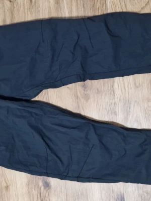 Nike byxor - Svarta byxor från Nike med vit logga på benet och elastisk midja med justerbart bälte. Byxorna har en avslappnad passform och är perfekta för chill eller träning. Materialet känns lätt och bekvämt. Nytt skick