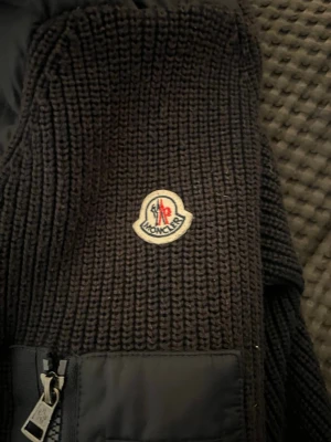 Marinblå cardigan från Moncler - Säljer en svart stickad jacka från Moncler med grov ribbstickning och en praktisk ficka med dragkedja framtill. Jackan har Monclers klassiska logga på bröstet och är perfekt för kyligare dagar och till den svenska våren. Skick 9/10 använt, Nft tag finns på både ärmen och intill. Tveka inte på att höra av dig pris kan diskuteras. 