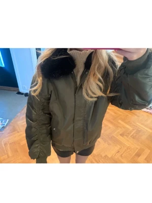 Olivgrön bomberjacka med fuskpäls - Snygg olivgrön bomberjacka med svart fuskpälsdetalj på kragen. Sååå fin❤️