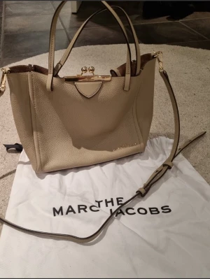 Beige handväska från Marc Jacobs - Marc Jacobs beige Mini The Kiss Lock Tote Superfin som ny, perfekt storlek passar med en liten laptop i lagom liten och lagom stor. Ca 33 cm bred 20 cm hög