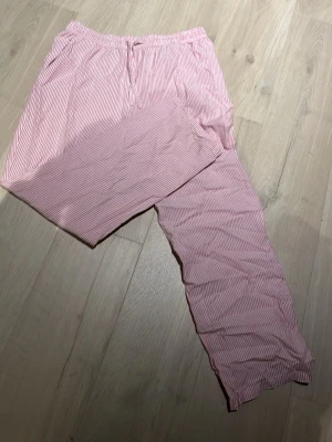 Rosa- och vitrandiga pyjamasbyxor - Säljer ett par pyjamasbyxor i mjukt tyg med rosa och vita smala ränder. Byxorna har resår i midjan och är långa i modellen, perfekta för mysiga hemmakvällar. Klassisk och enkel design som passar alla.