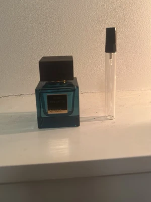 Rituals parfymflaska blå - Snygg parfym från rituals i en elegant blå glasflaska med svart fyrkantigt lock och guldfärgad etikett. Medföljer även ett genomskinligt provrör med svart spraykork. Perfekt för dig som gillar exklusiva dofter och stilren design.