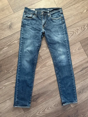 Levi's 511 blå jeans herr - Säljer ett par klassiska blå Levi's 511 jeans med smal passform och normal midja. Jeansen har fem fickor, dragkedjegylf och snygga slitningar på låren för en avslappnad look. Perfekta till vardags och passar till det mesta.