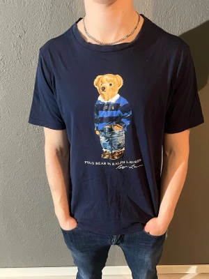 Mörkblå Polo Bear t-shirt Ralph Lauren - Snygg mörkblå t-shirt från Ralph Lauren med den ikoniska Polo Bear-trycket på bröstet. T-shirten har rund hals och korta ärmar. Storleken är S men passar M då den är stor i storleken. Riktigt fet t-shirt som är mycket eftertraktad och aldrig går fel. Skick 9/10. Vid minsta fundering så är det bara att höra av sig💙