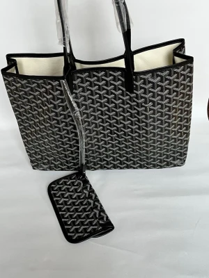 Svart shoppingväska med mönster - Snygg svart shoppingväska från Goyard med ikoniskt grafiskt mönster i vitt och grått. Väskan har två svarta handtag och medföljande liten avtagbar innerficka. Insidan är ljus och väskan är rymlig, perfekt för alla dina grejer.