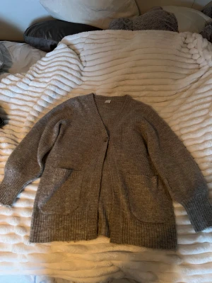 Grå ribbstickad kofta från Lindex - Mysig grå ribbstickad kofta från Lindex med två stora fickor framtill och v-ringad hals. Storleken som står är 134/140 men skulle säga att den är XS! Perfekt för lager-på-lager och har långa ärmar samt en enkel knappstängning. Snygg och enkel att matcha till det mesta. 