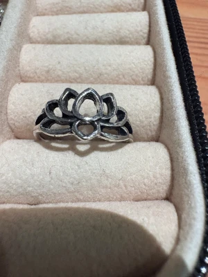 Lotusring i silverfärgad metall - Unik ring med lotusblomma-design i silverfärgad metall. Ringen har öppna detaljer och en cool, bohemisk vibe som sticker ut. Perfekt för dig som gillar statement-smycken och vill ha något som känns personligt och stilrent.
