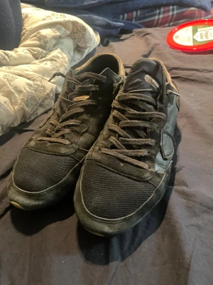 Svarta phil modell i mocka och textil - Svarta sneakers med ovandel i mocka och textil, klassisk snörning och rund tå. Sulan är ljusbrun och har ett tydligt mönster undertill. Skorna har en stilren och enkel design som passar till många outfits.