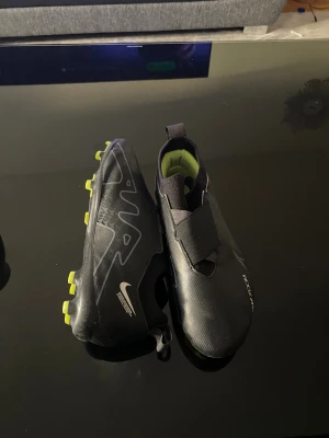 Nike Mercurial fotbollsskor svart/gul - Säljer ett par Nike Mercurial fotbollsskor i svart med neongula dobbar och detaljer. Skorna har en slimmad design med täckt snörning och elastiskt band över vristen. Insidan är fodrad i limegrönt tyg och yttermaterialet är syntet för bästa grepp och känsla på planen.